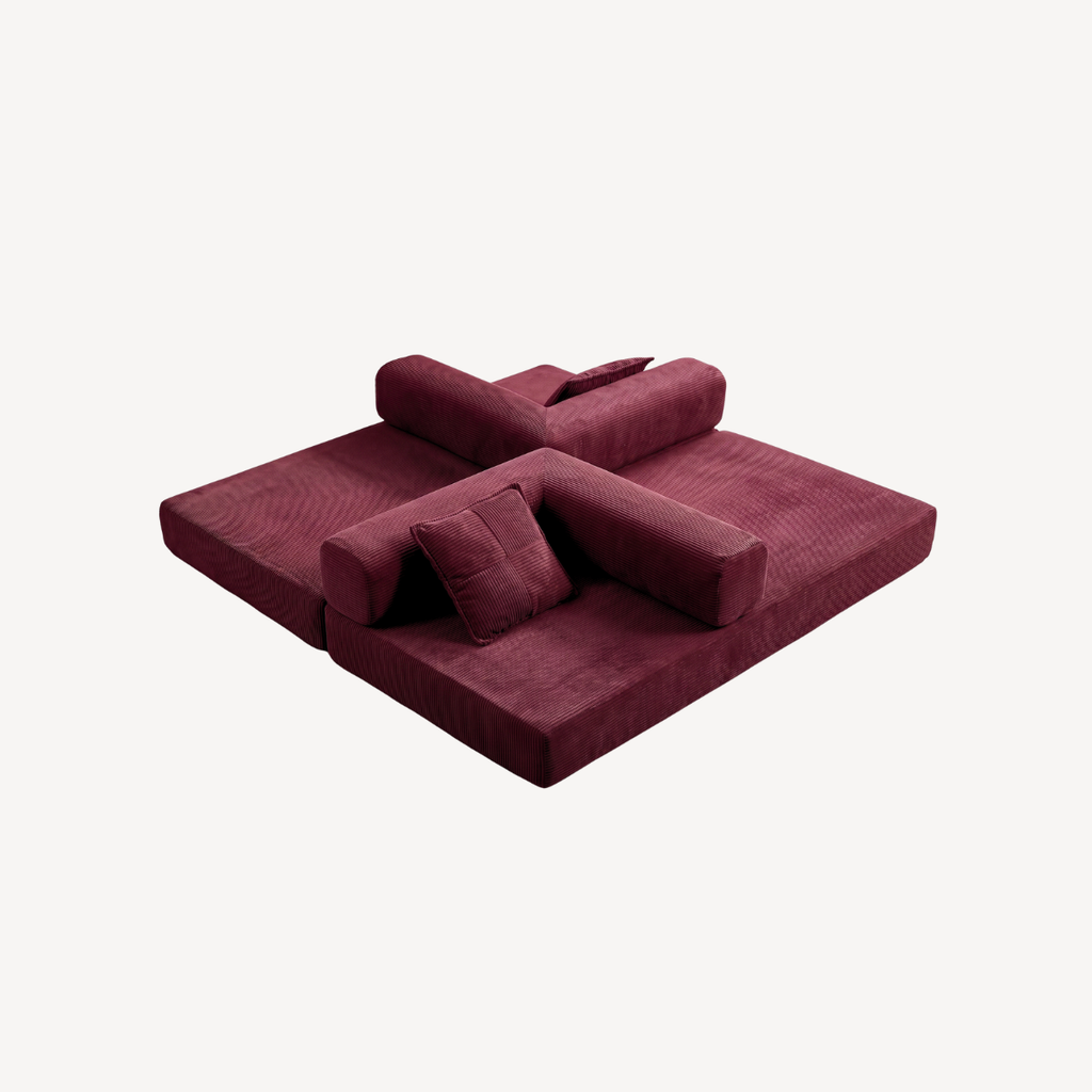 Canapé modulable bordeaux en velours côtelé, couchage déployé avec coussins empilés.