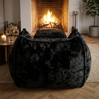 Fauteuil en fourrure noire très épaisse avec repose-pied, forme enveloppante.